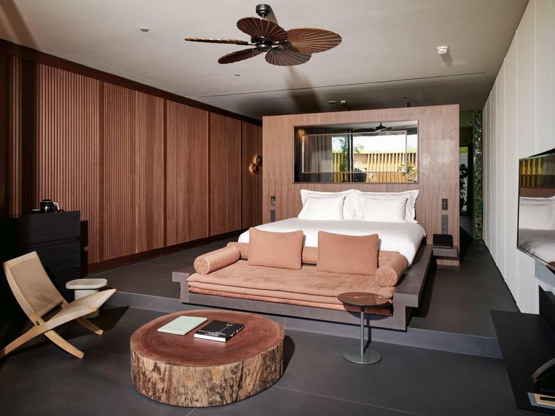 Habitación de hotel moderna con paredes de madera, mesa de centro rústica y ventilador de techo.