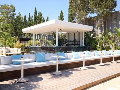 Área exterior moderna con sofás blancos y mesas en terraza de madera junto a bar bajo toldo.