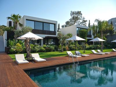 Casa moderna con piscina e ombrelloni in giardino soleggiato e verde.