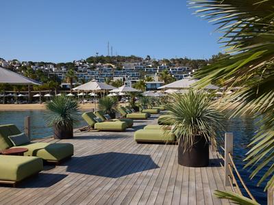Sonnendeck mit grünen Liegen und Blick auf Wasser und Hügel mit Häusern