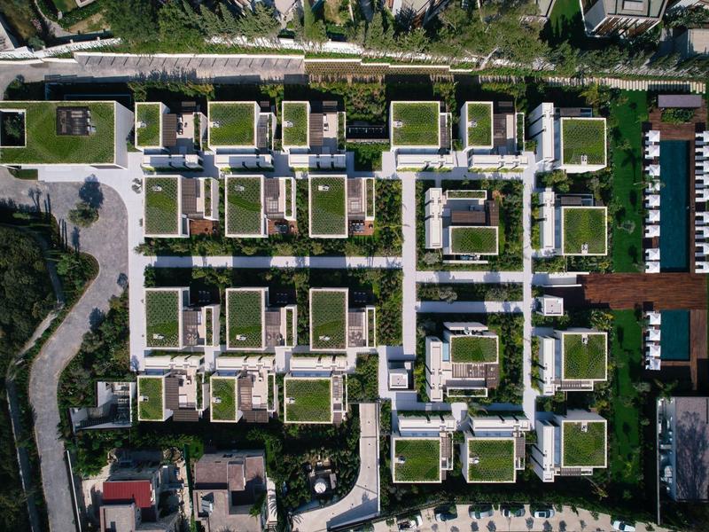 Vista aérea de un complejo hotelero moderno con edificios cuadrados, techos verdes y un muelle para botes.
