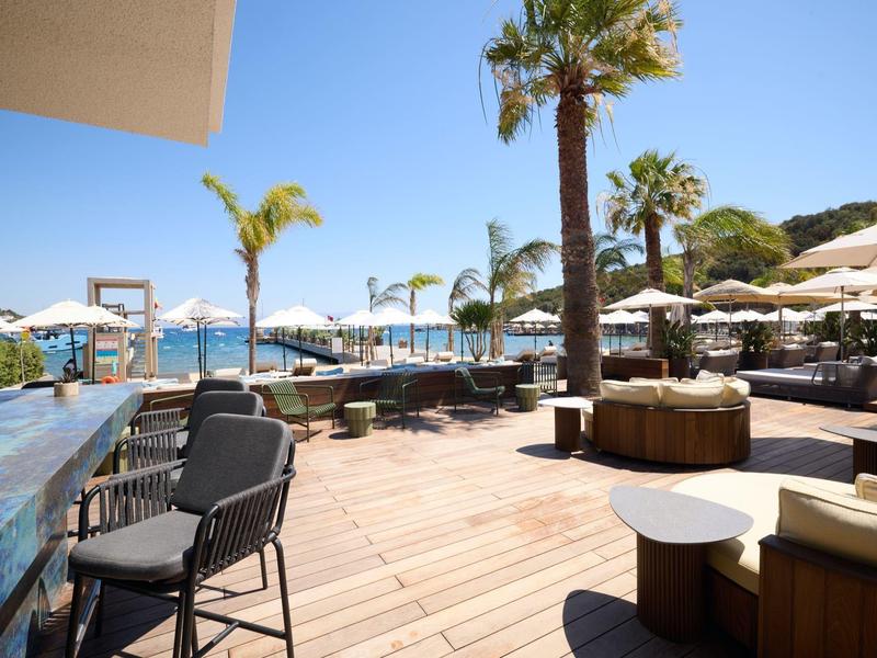 Amplia terraza de hotel con suelo de madera, sillas, sombrillas y vista al mar bajo cielo azul.