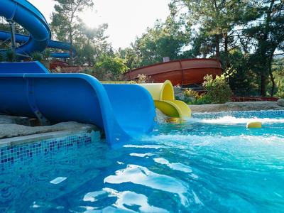 Niebieskie i żółte zjeżdżalnie wodne prowadzące do basenu z czystą wodą otoczonego drzewami.