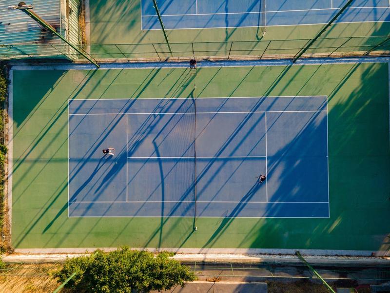 Widok z lotu ptaka na pusty kort tenisowy z długimi cieniami ogrodzenia.