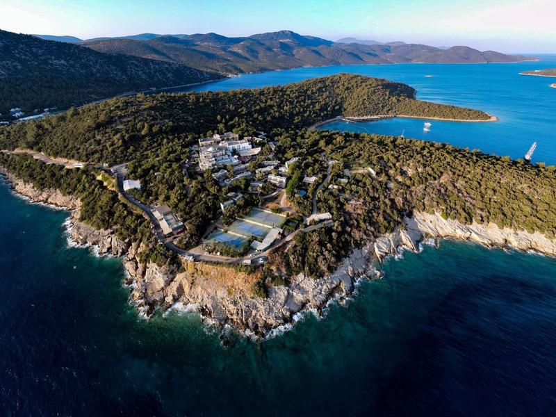 Widok z lotu ptaka na kompleks hotelowy na zalesionym półwyspie z widokiem na niebieskie morze.