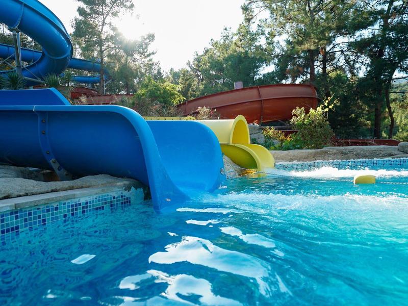 Niebieskie i żółte zjeżdżalnie wodne prowadzące do basenu z czystą wodą otoczonego drzewami.