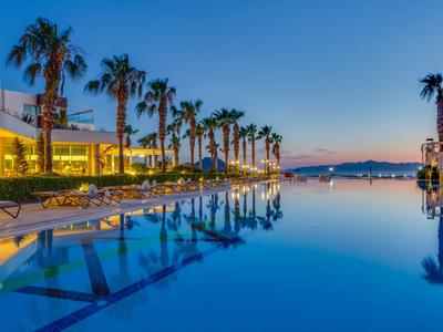 Piscine à débordement avec palmiers et chaises longues au coucher du soleil près de l'hôtel de plage.