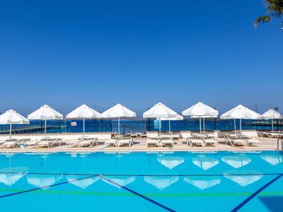 Rangées de parasols blancs et de chaises longues autour de la piscine avec vue sur la mer.