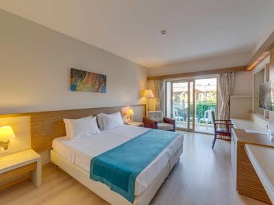 Bright hotel room with double bed, desk, and balcony access overlooking the garden.