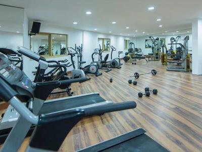 Grande salle de sport avec sol en bois, haltères et divers équipements d'entraînement.