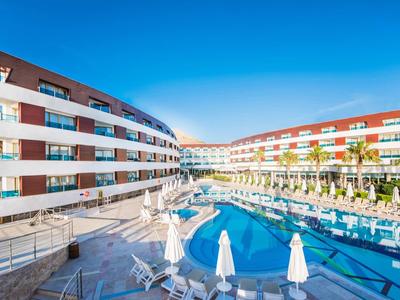 Moderner Apartmentkomplex mit blauem Pool, weißen Sonnenschirmen und klarem Himmel.