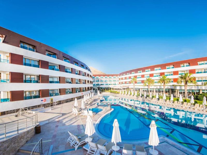 Modern hotel complex with pool between two buildings under clear blue sky.