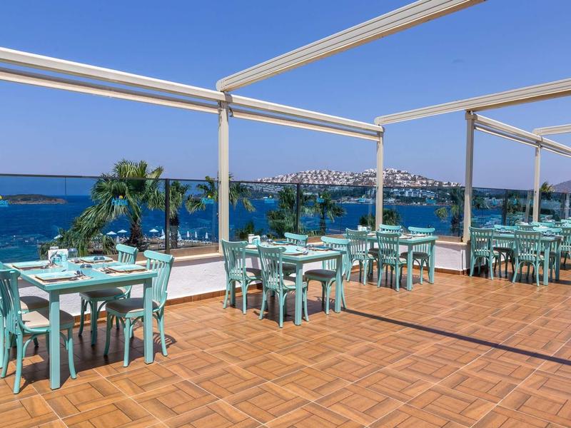 Open terrace with tables and chairs, overlooking the sea and a coastline in the background.