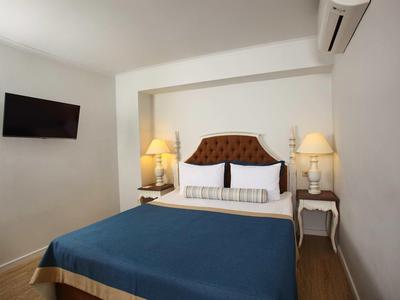 Camera d'hotel accogliente con letto matrimoniale, comodini e TV a parete.