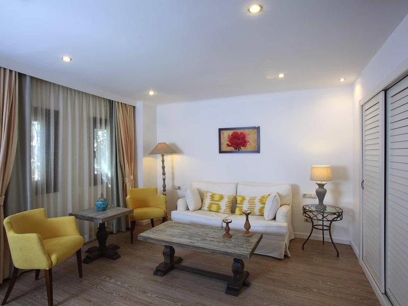 Soggiorno accogliente con poltrone gialle, divano bianco e tavolo in legno in una camera d'hotel.