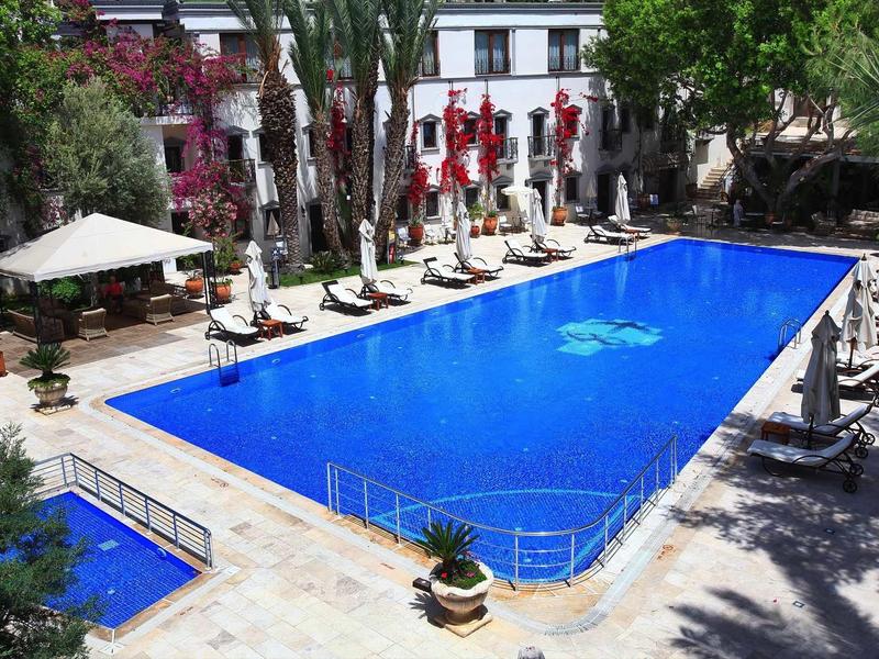 Una grande piscina rettangolare circondata da lettini e ombrelloni in un giardino dell'hotel.