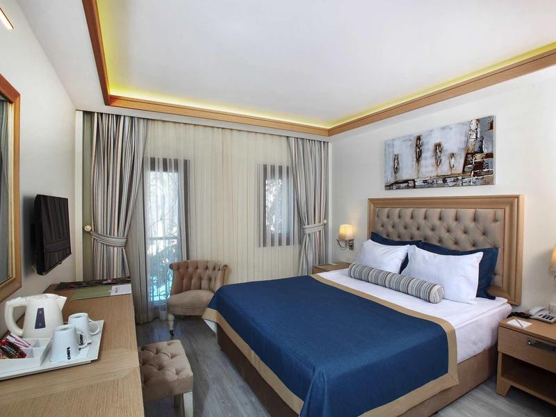 Camera d'hotel moderna con letto blu, poltrona, scrivania, TV e macchina per il caffè.