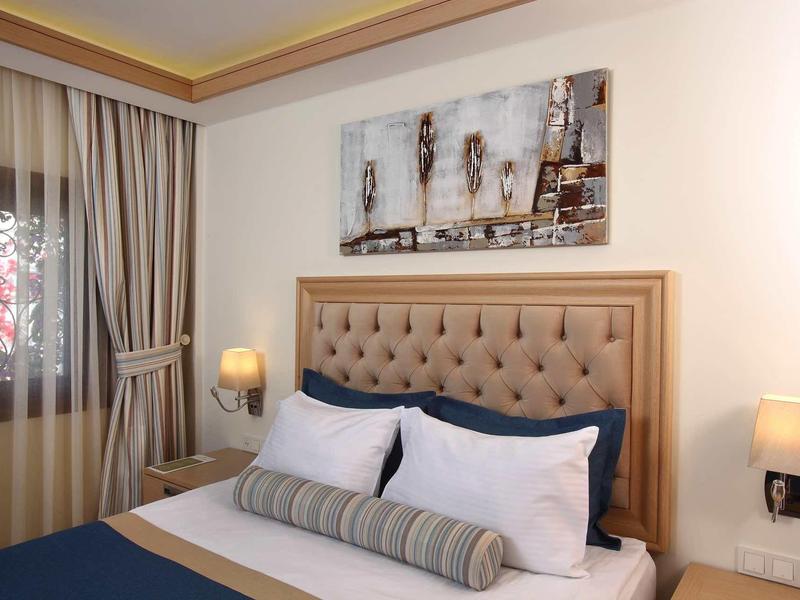 Camera d'albergo accogliente con testata imbottita, lampade da comodino e decorazione murale.