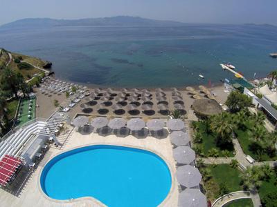 Strand mit blauem Pool, Sonnenschirme, Strandliegen und ruhigem Meer im Hintergrund.