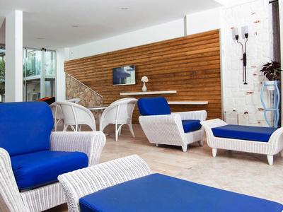 Zona lounge moderna con mobili in vimini bianco e cuscini blu davanti a parete in legno.