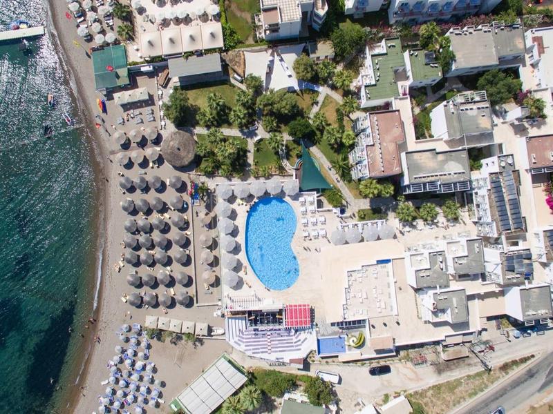 Vista aerea di un hotel con piscina all'aperto e ombrelloni vicino al mare.