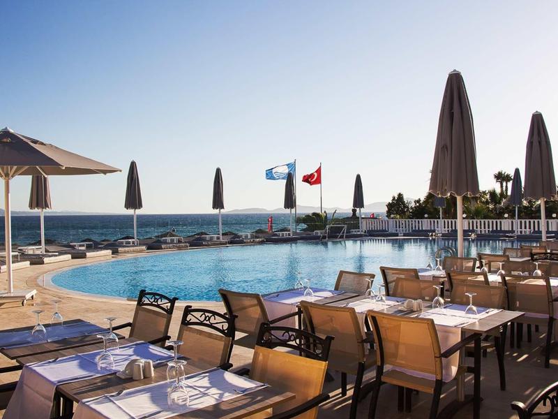 Terrazza dell'hotel con tavoli da pranzo accanto a una piscina con vista sul mare e ombrelloni.