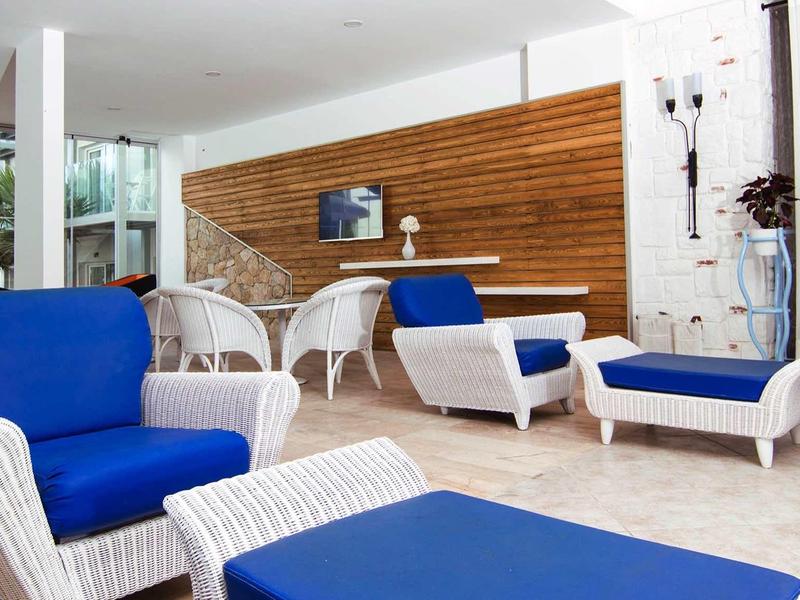 Zona lounge moderna con mobili in vimini bianco e cuscini blu davanti a parete in legno.