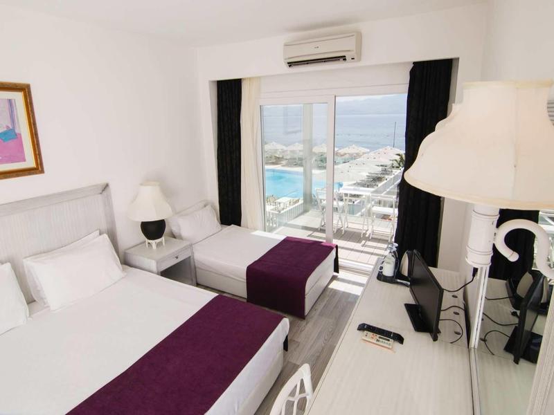 Camera d'hotel moderna con due letti, arredi bianchi e vista sul porto.