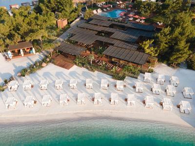 White lounge chairs with umbrellas on the beach in front of a resort with pool and trees
