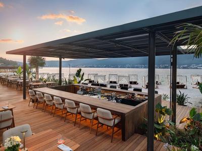 Modern outdoor bar area with sea and mountain view at sunset.