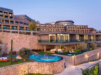 Modern hotel with multiple floors and outdoor pool surrounded by stone walls.