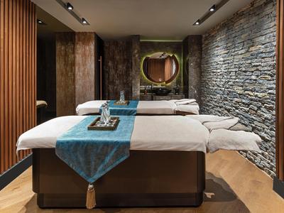 Cozy spa room with two massage tables, mood lighting, and natural stone wall accents.
