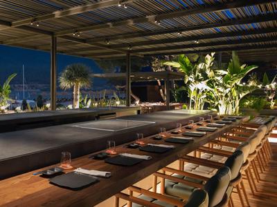Modern restaurant with wooden chairs and set tables under covered outdoor area at night.