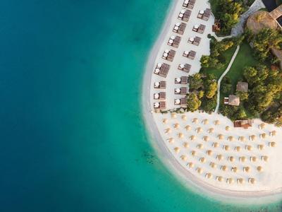Aerial view of a beach with loungers and umbrellas beside clear blue water.