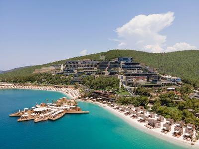 Luxury beach resort by turquoise sea with sun umbrellas and green hill in the background.
