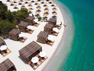 Plaża z drewnianymi bungalowami i białymi parasolami obok przejrzystej turkusowej wody.