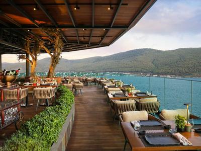 Restaurant terrace overlooking the sea and wooded hills at sunset.