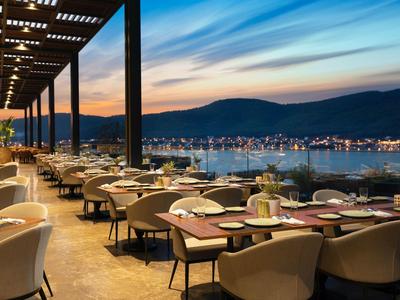 Rooftop restaurant overlooking harbor and mountains at sunset.