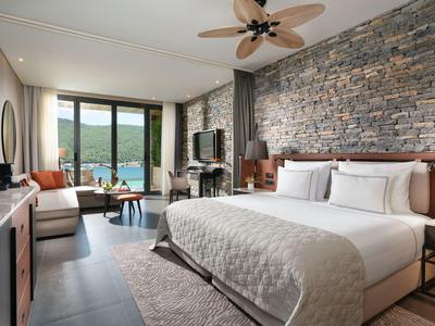 Nowoczesny pokój hotelowy z dużym łóżkiem, kamienną ścianą i widokiem na jezioro i góry