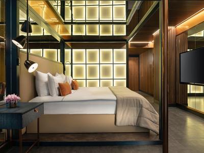 Modern hotel room with large bed, decorative headboard, and indirect lighting.