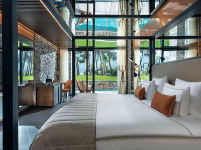 Elegant hotel room with large bed, glass walls, and garden view.