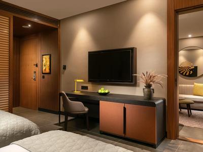 Modern hotel room with TV, desk, and cozy sitting area in the background.