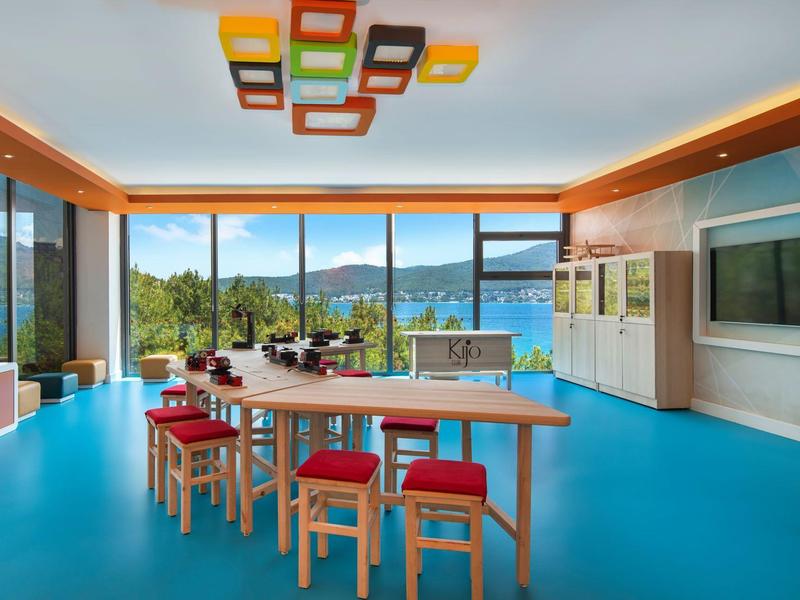 Modern dining room with large wooden table, red chairs, and panoramic windows overlooking the lake.