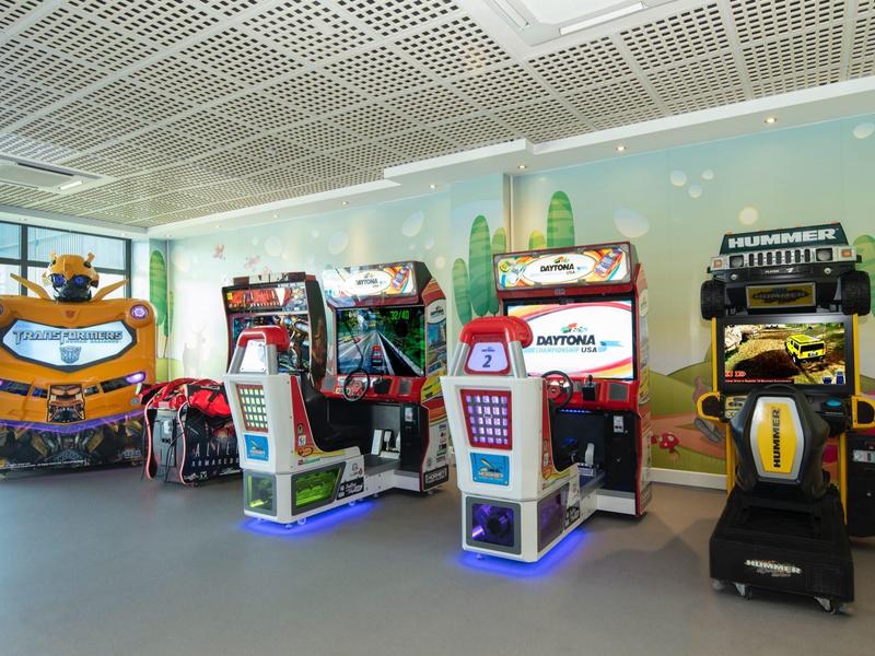Arcade room with various racing and driving simulator machines in a bright space.