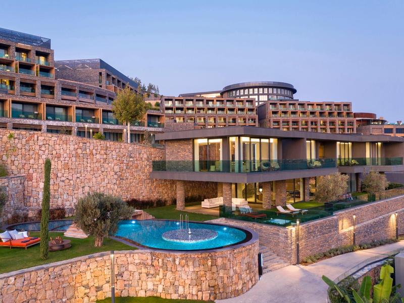 Modern hotel with multiple floors and outdoor pool surrounded by stone walls.