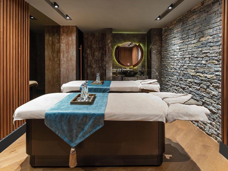 Cozy spa room with two massage tables, mood lighting, and natural stone wall accents.