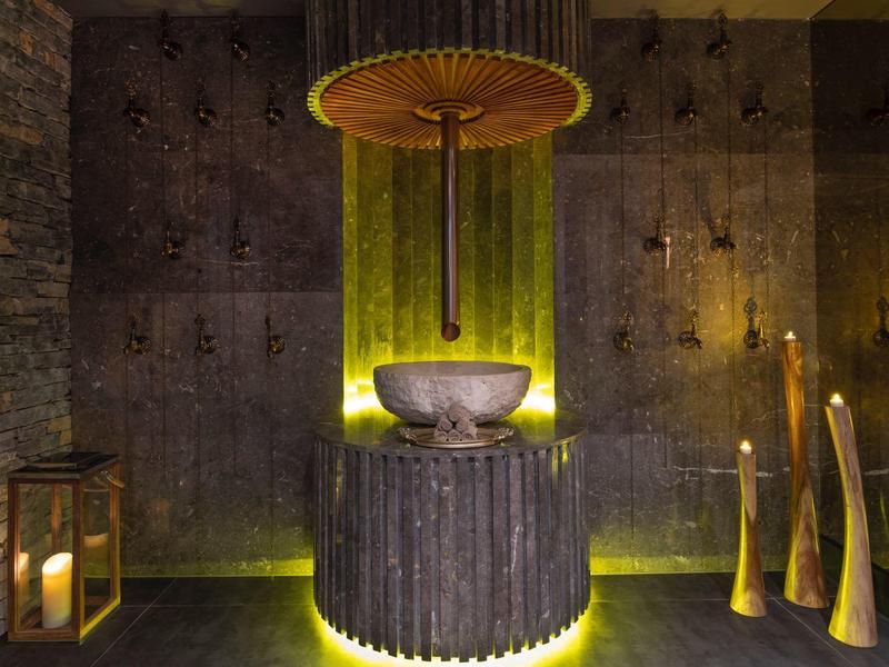 Atmospheric hotel bathroom fountain with dark stone and warm lighting.