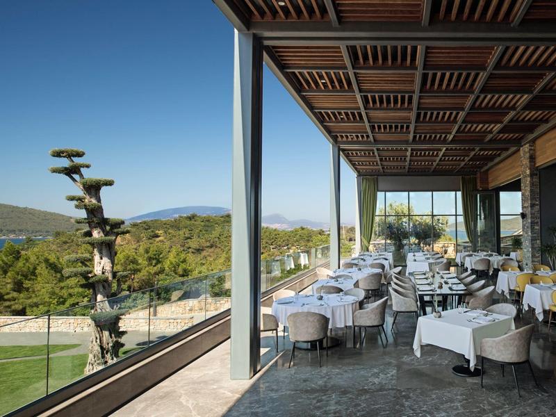 Modern outdoor restaurant area with set tables and views of hills and a lake.