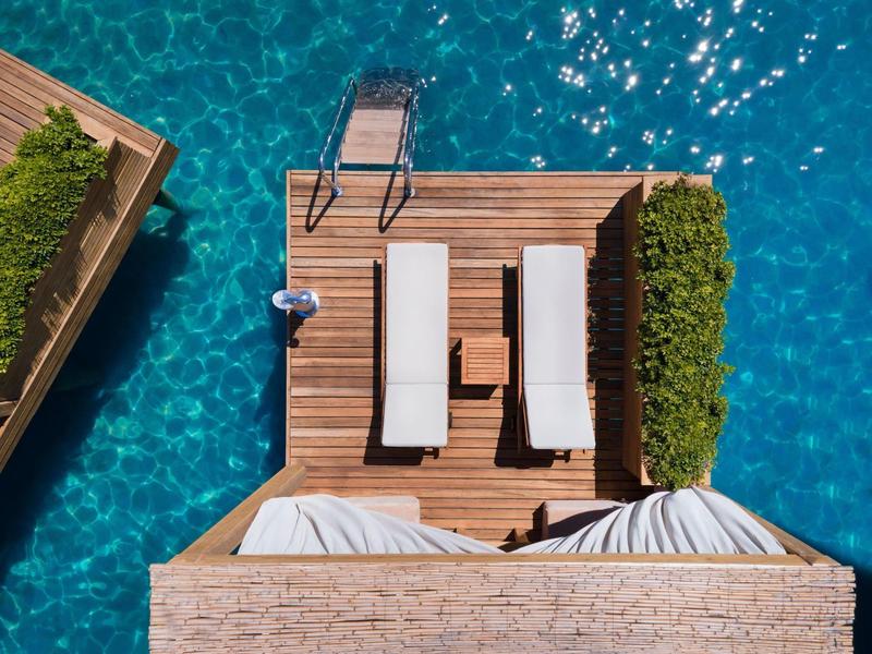 Top-down view of wooden deck with lounge chairs next to turquoise water.