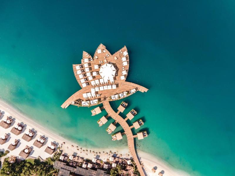 Aerial view of a tropical resort with pools and bungalows over turquoise water.